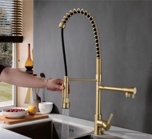Gold kitchen faucet with flexible hose being adjusted by a person in a kitchen setting.